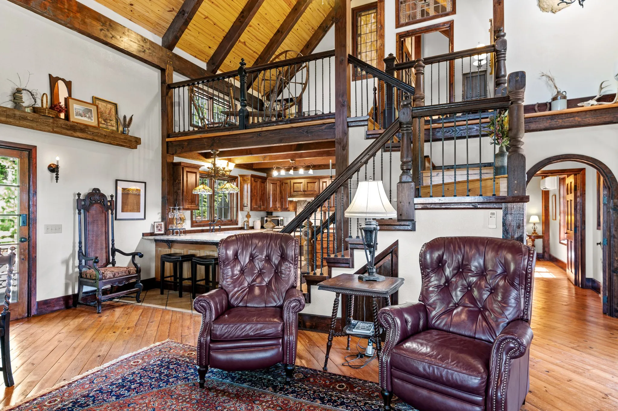 Multi-Level Living Space Open-concept living area with loft view, leather furniture, wooden beams, and iron railing