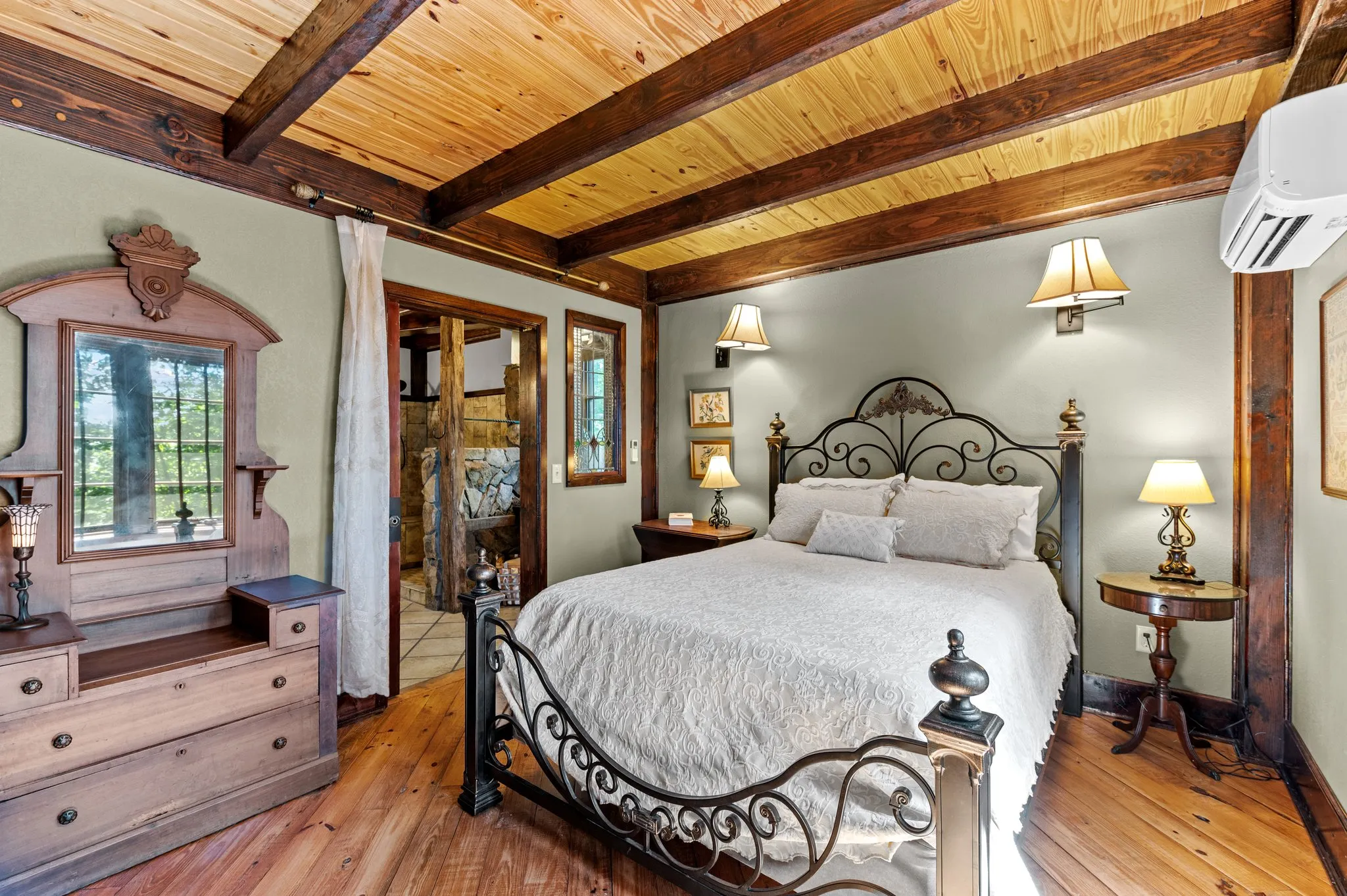 Downstairs Bedroom Downstairs bedroom with ornate iron bed frame, wood beams, bedside tables, and sitting area by windows