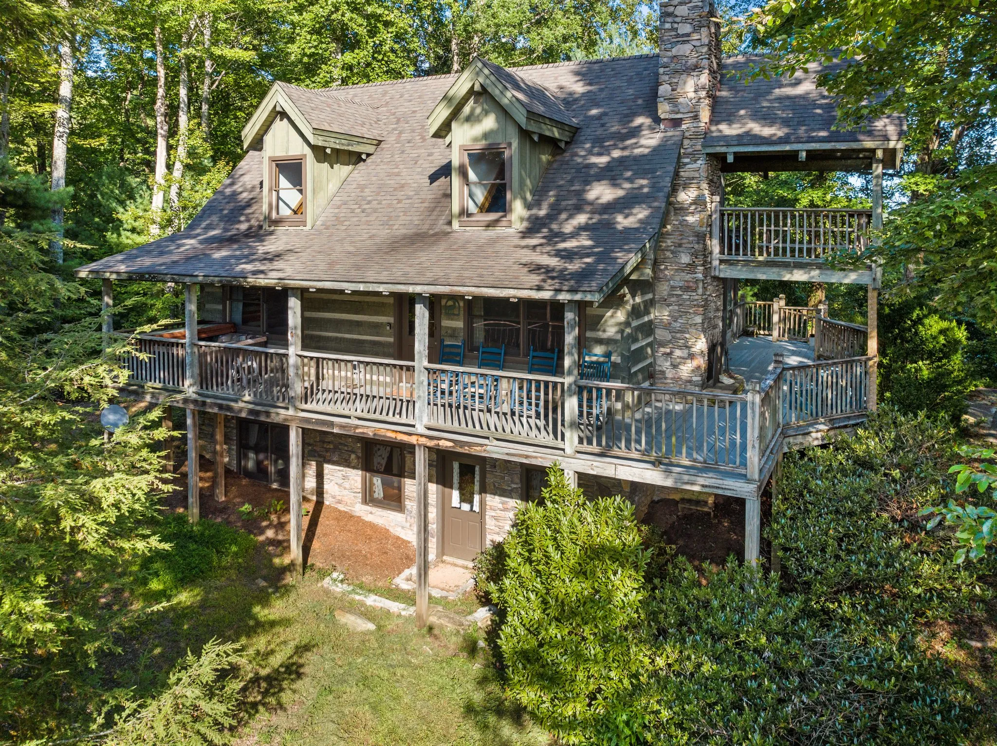 Aerial view of log cabin showing multiple decks, peaked roof, and secluded forest setting