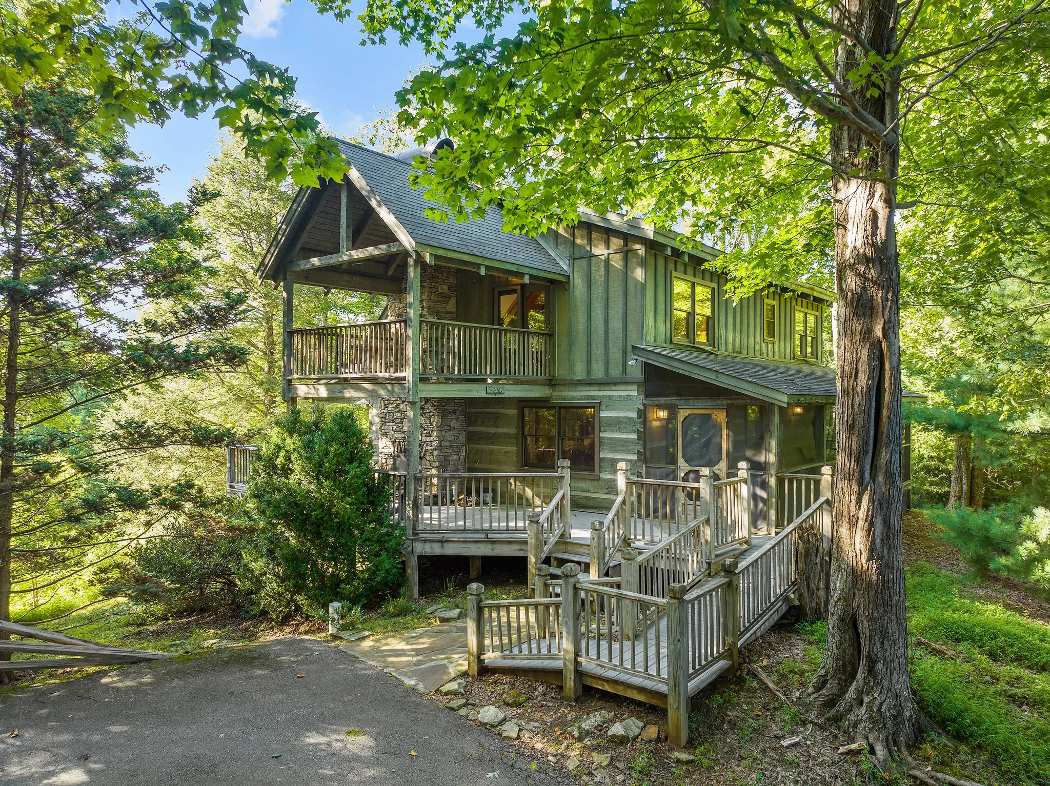 Front view of log cabin with stone foundation, staircase entry, and spacious upper and lower decks