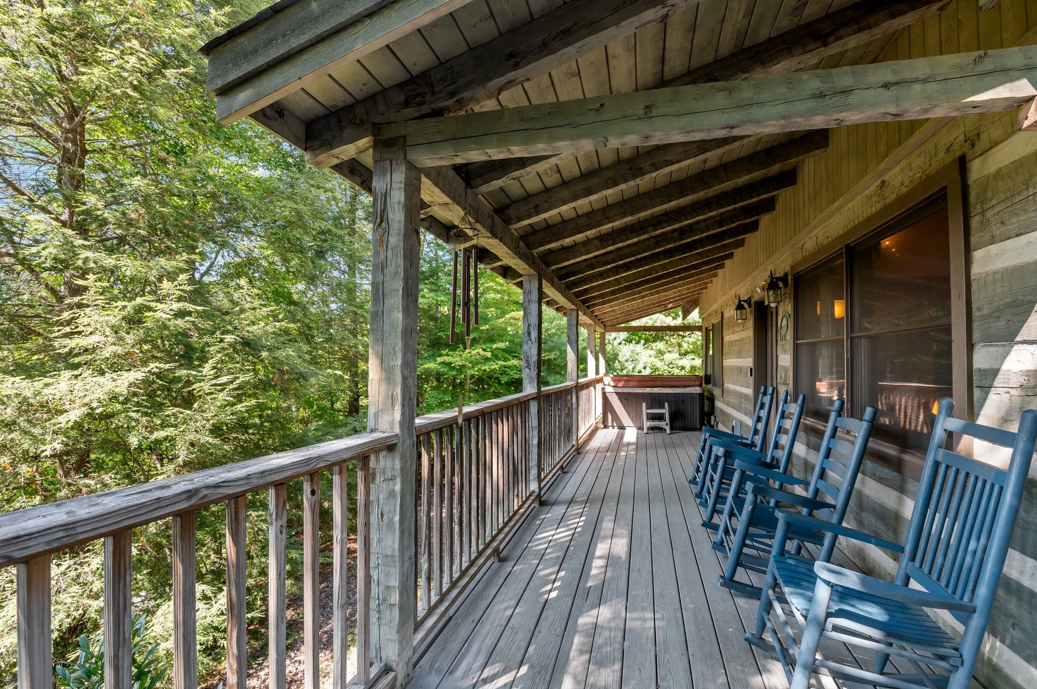 Spacious covered porch with blue rocking chairs, dining table, and forest views