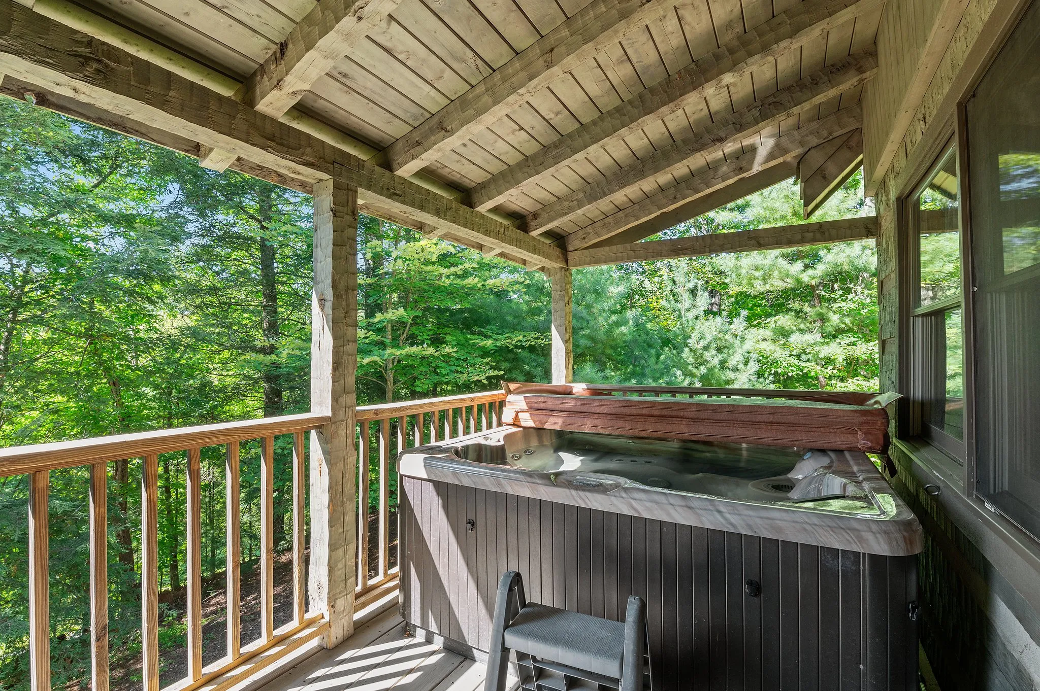 Hot tub on covered deck with timber beam ceiling surrounded by forest greenery