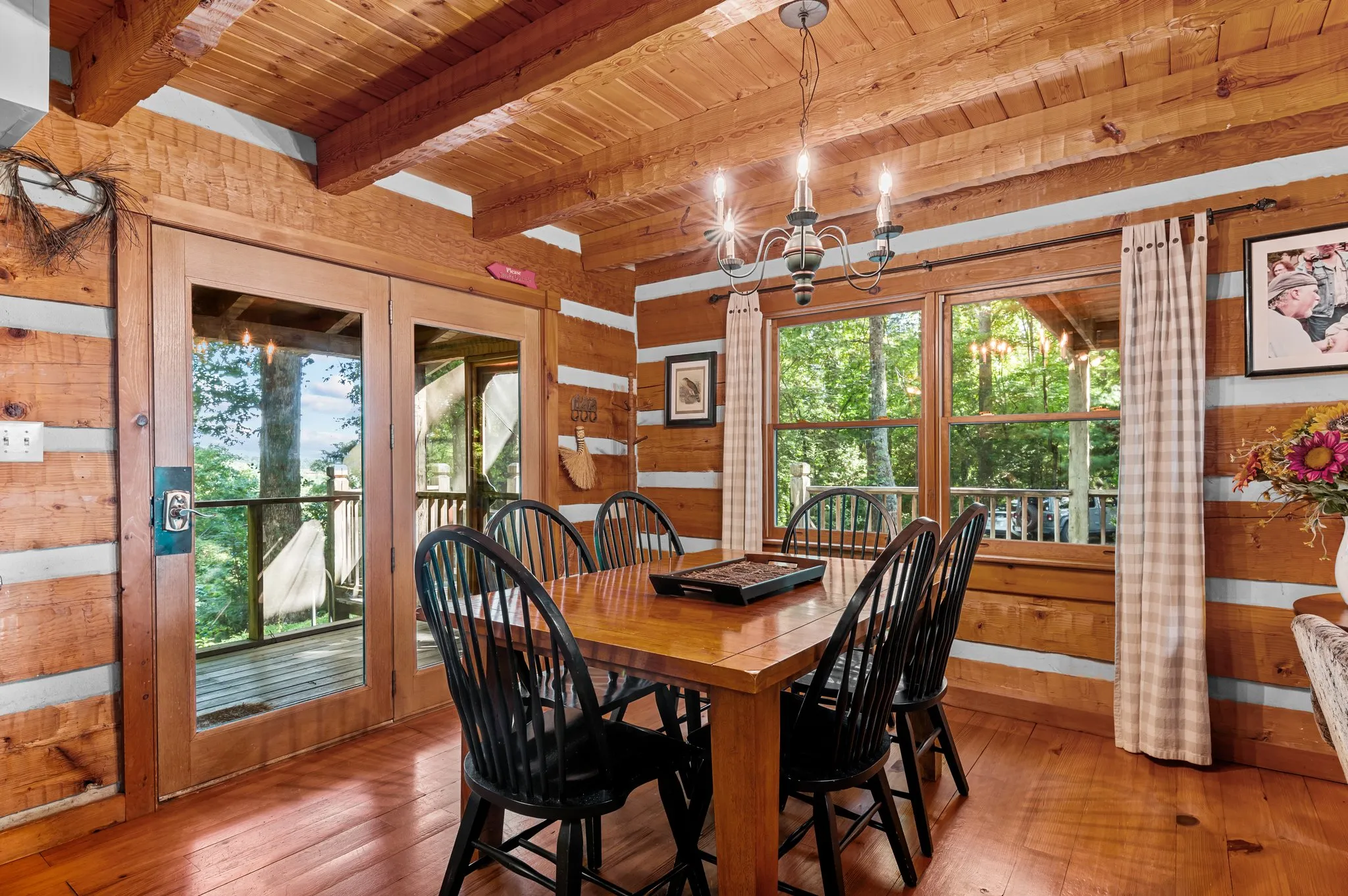 Dining room with rustic log walls, Windsor chairs, chandelier, and glass doors to deck