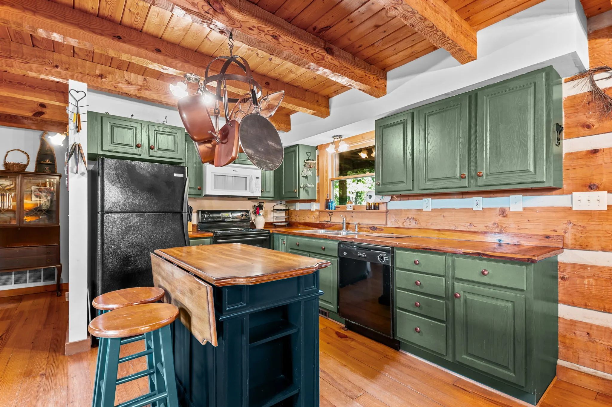 Country kitchen with green cabinets, wood countertops, island with bar stools, and hanging pot rack