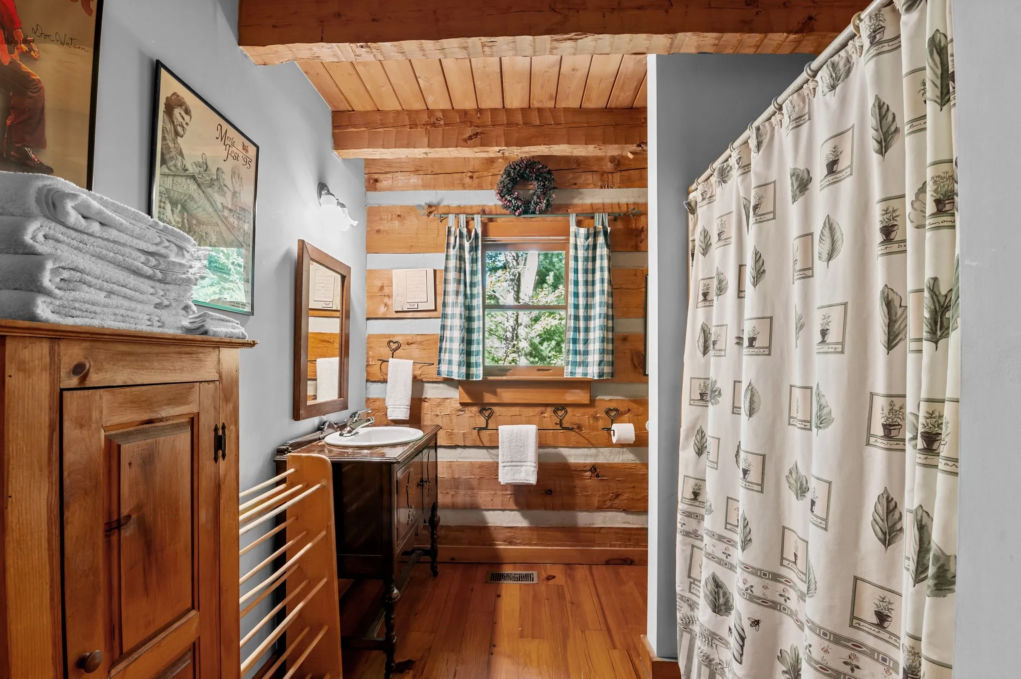 Rustic bathroom with log walls, pedestal sink, vintage botanical shower curtain, and stained glass window