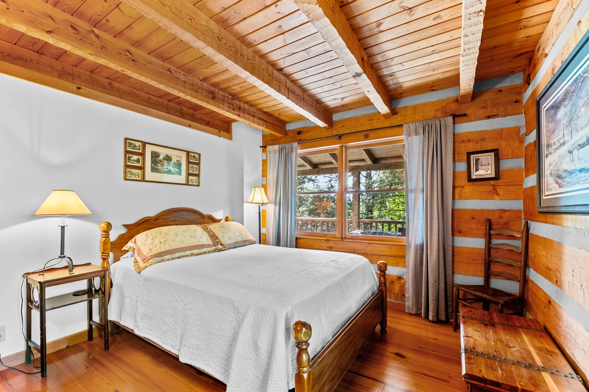 Cozy bedroom with vaulted wood ceiling, iron bed frame, hardwood floors, and forest views