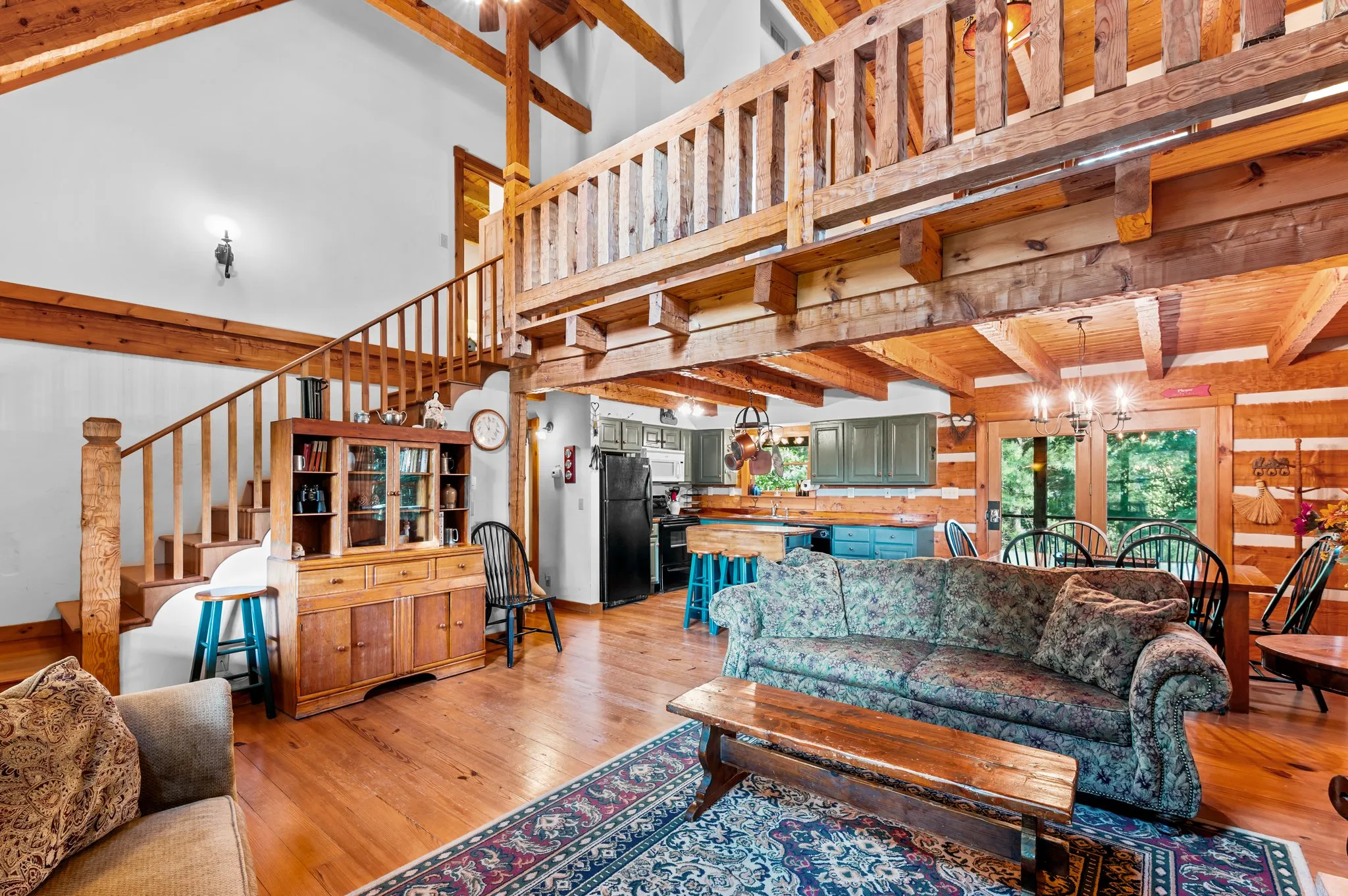 Open concept living area showing loft staircase, green kitchen cabinets, and log beam construction