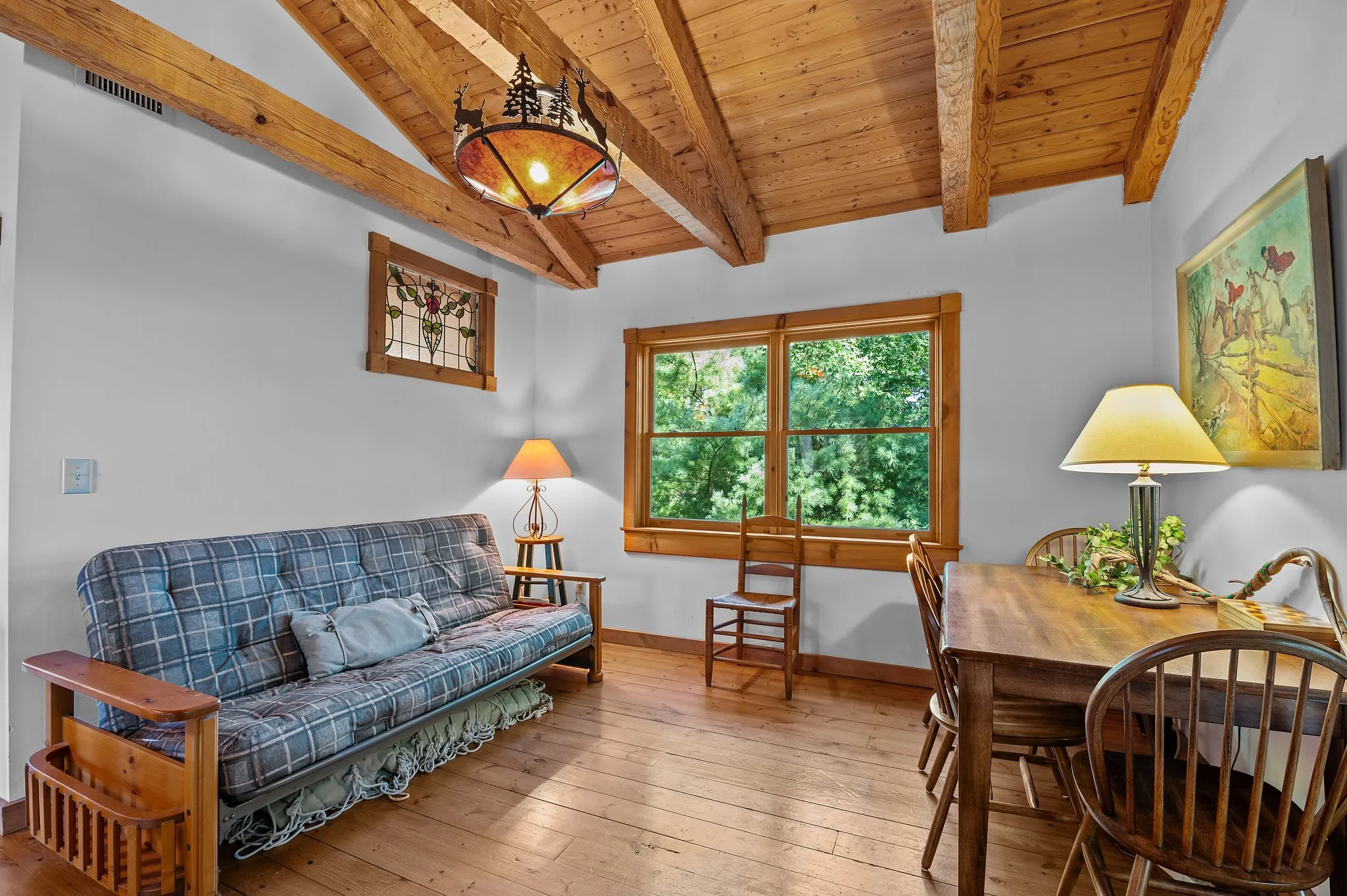 Multi-purpose guest room with futon, dining table, exposed beams, and rustic chandelier