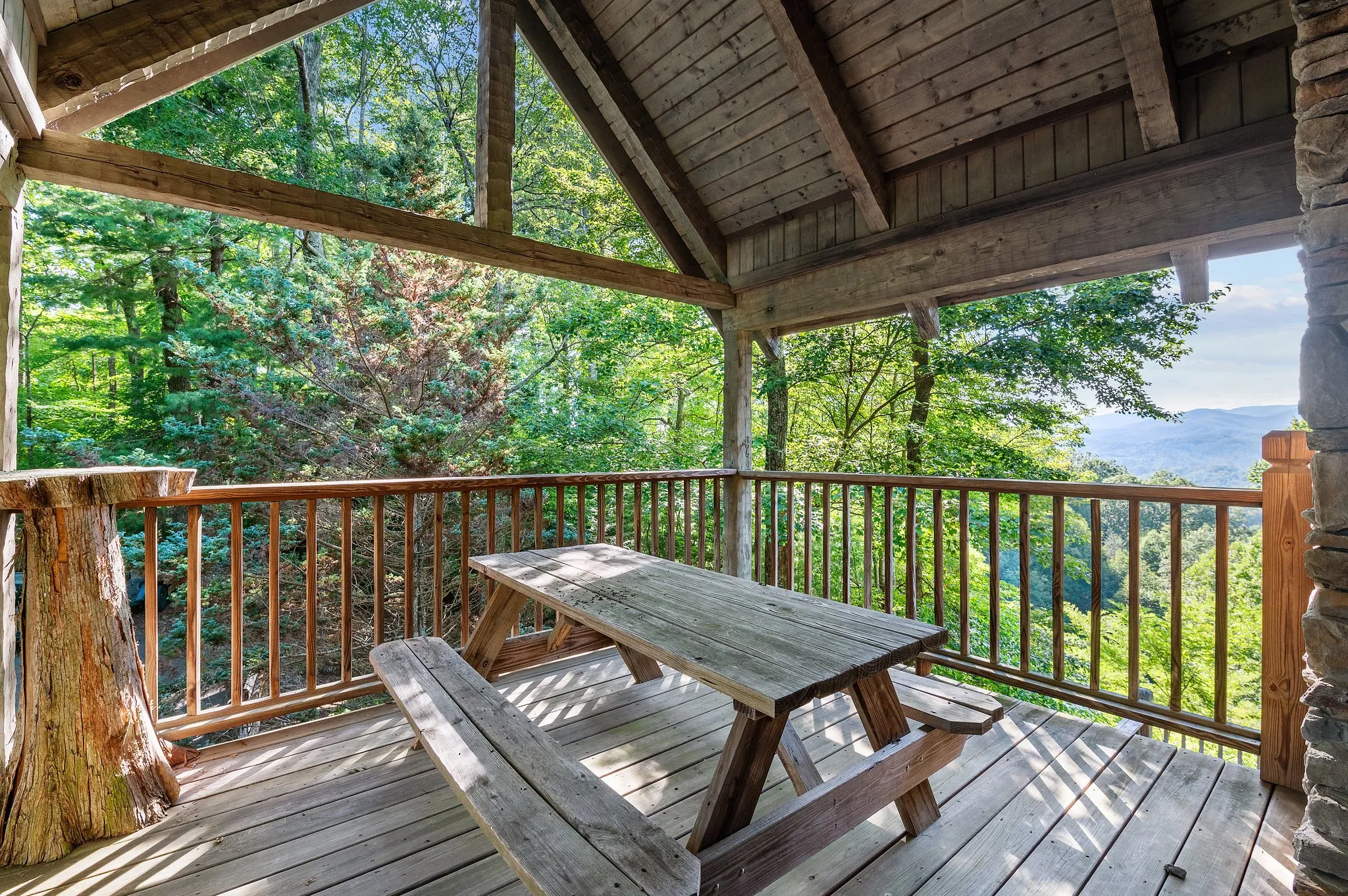 Covered deck with picnic table and sweeping mountain valley views through forest trees