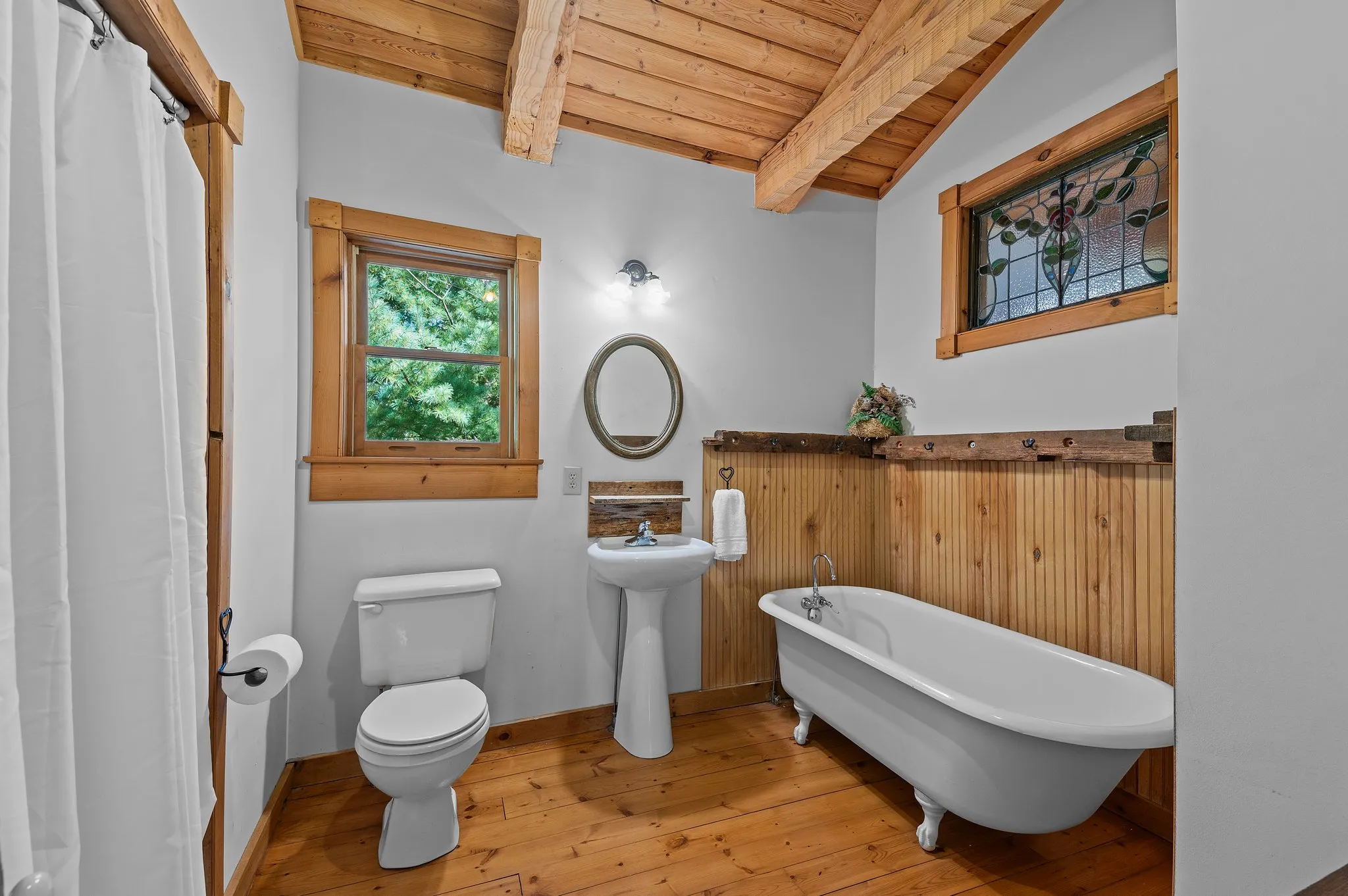 Charming bathroom featuring white clawfoot tub, wood wainscoting, pedestal sink, and stained glass window