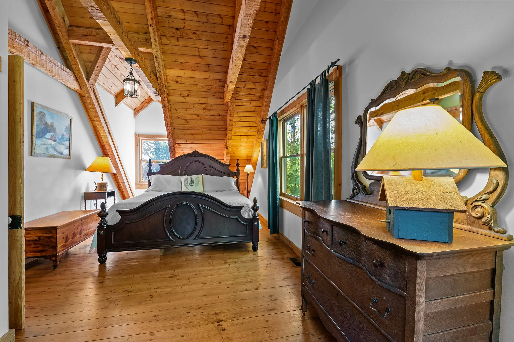 Spacious upstairs bedroom with vaulted ceiling, dark wood bed, antique dresser with ornate mirror