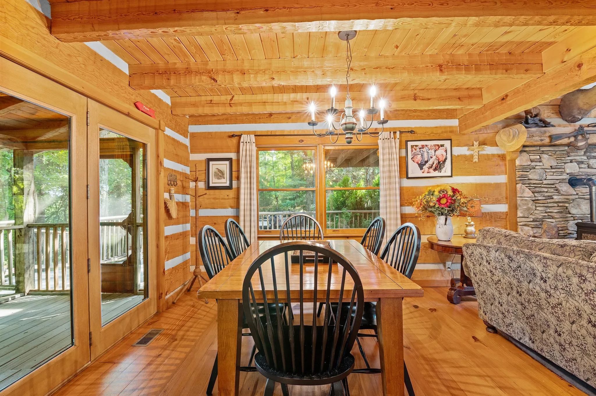 Main level dining area with log walls, stone fireplace accent, and glass doors to deck