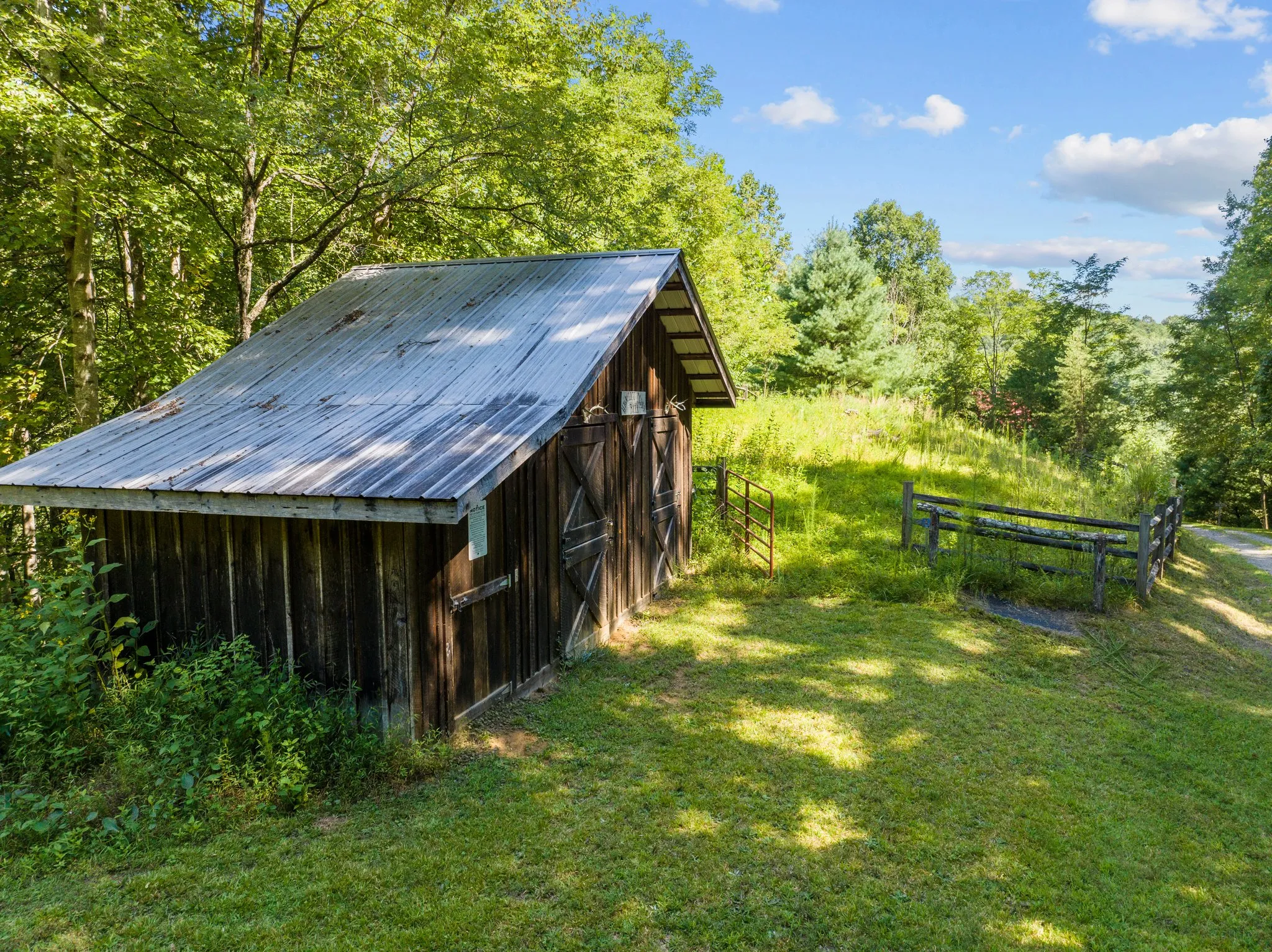 Weathered wooden barn with metal roof on grassy hillside surrounded by trees