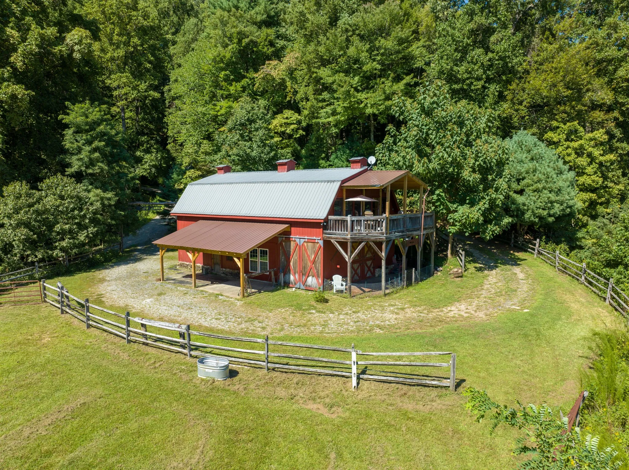Overhead view of barndominium with split rail fence enclosure in forest clearing
