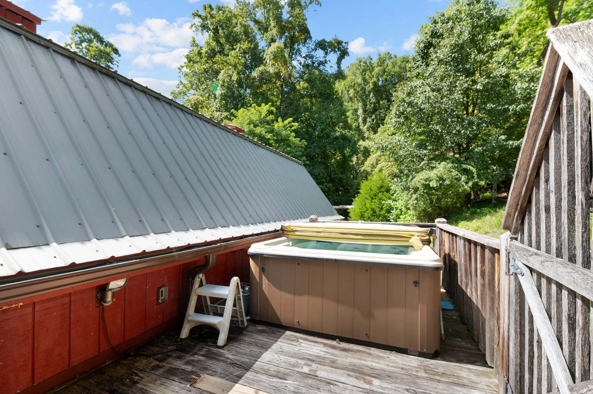 Hot tub on wooden upper deck surrounded by forest canopy with metal barn roof