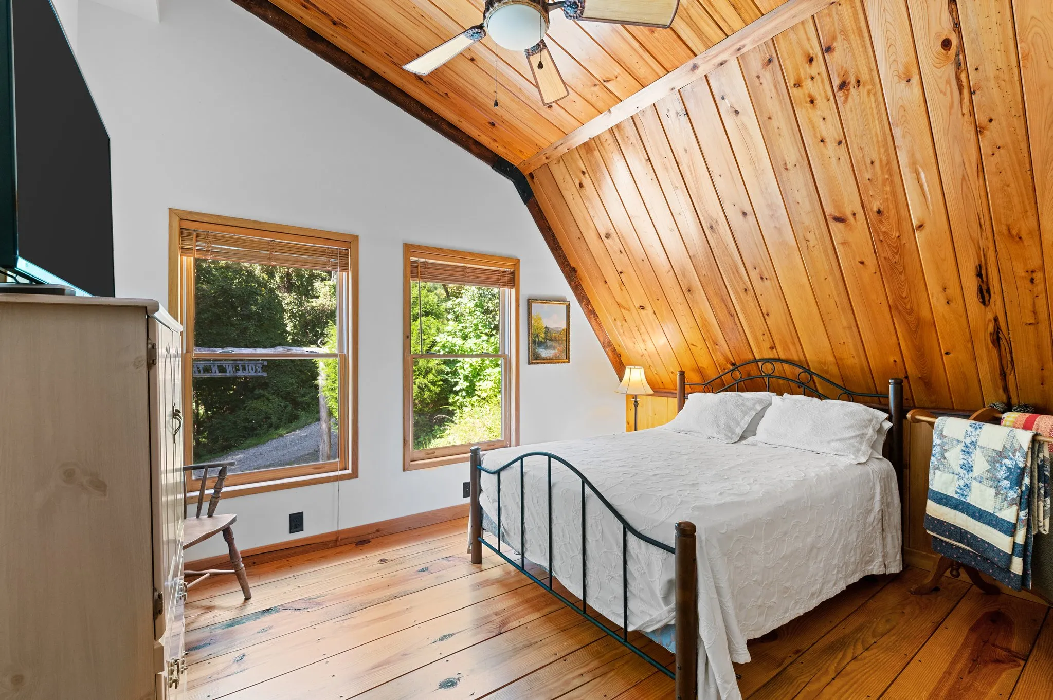 Cozy bedroom with vaulted wood ceiling, iron bed frame, hardwood floors, and twin windows
