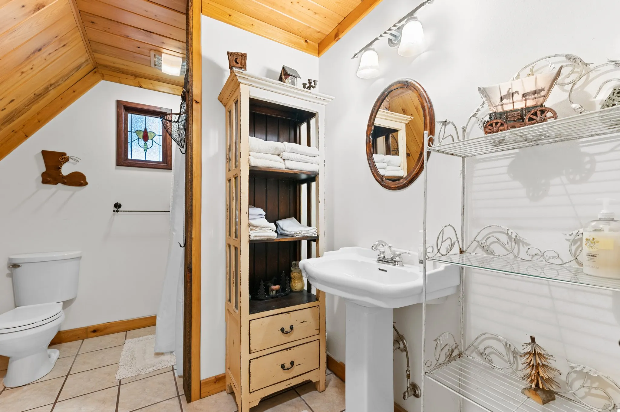 Rustic bathroom with pedestal sink, antique linen cabinet, stained glass window, and wagon wheel decor