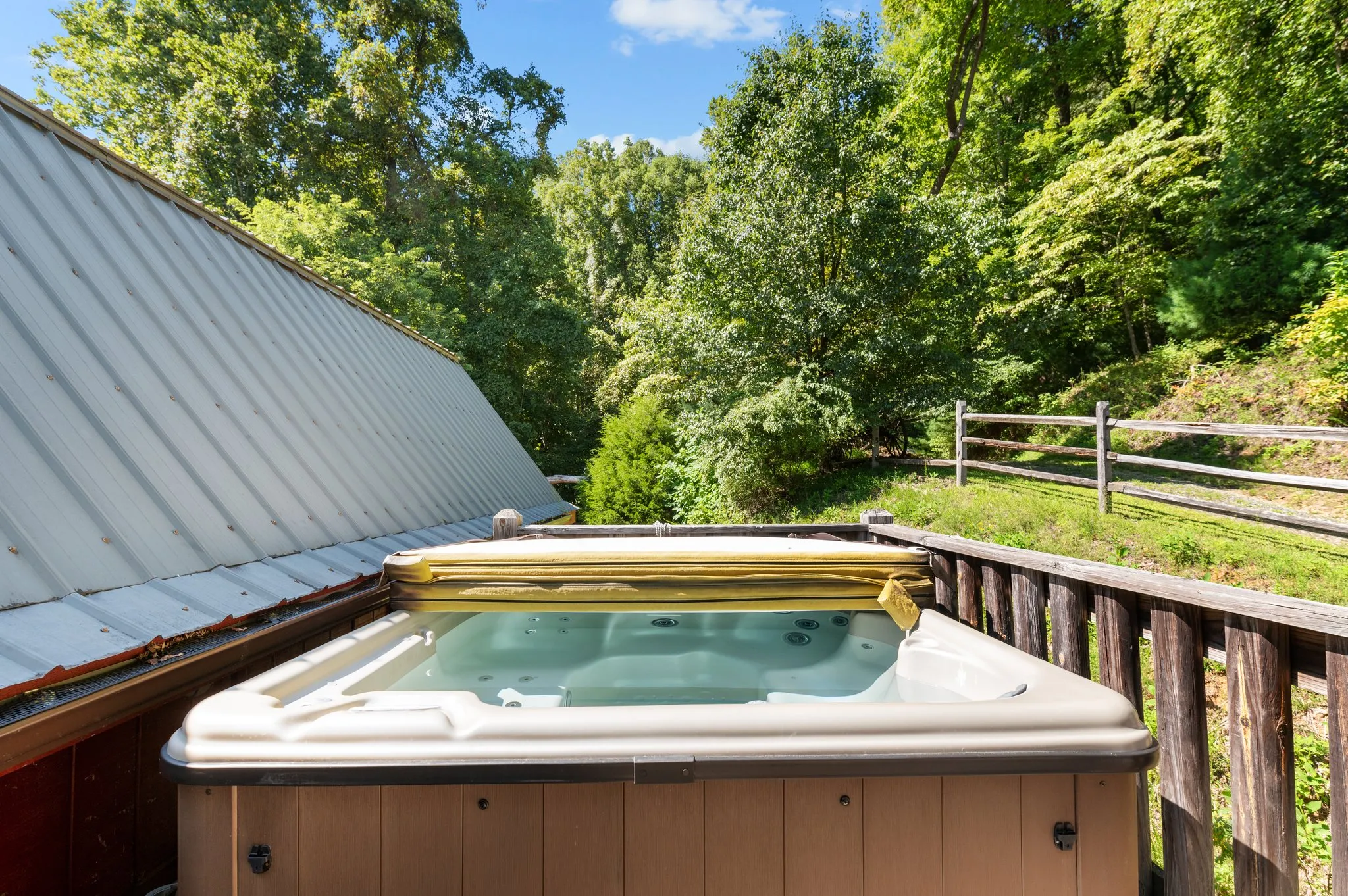 Hot tub on lower deck with wooden railing surrounded by lush forest and mountain landscape
